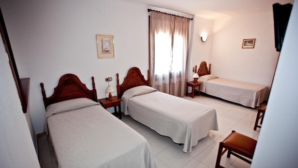 Ein Hotelzimmer mit zwei Einzelbetten, einem kleinen Tisch, einem Stuhl und einem Fenster mit Vorhängen.