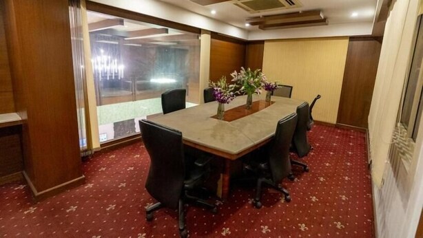 Un salón de conferencias con una larga mesa, sillas y un jarrón de flores.