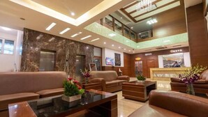 Vestíbulo de hotel con una recepción, zona de estar y una escalera que lleva a un nivel superior.