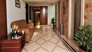 Un hall de hotel con mostrador de recepción, un sofá, una planta en maceta y una pared de mármol.
