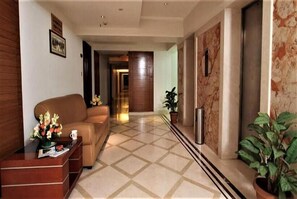 Un hall de hotel con mostrador de recepción, un sofá, una planta en maceta y una pared de mármol.