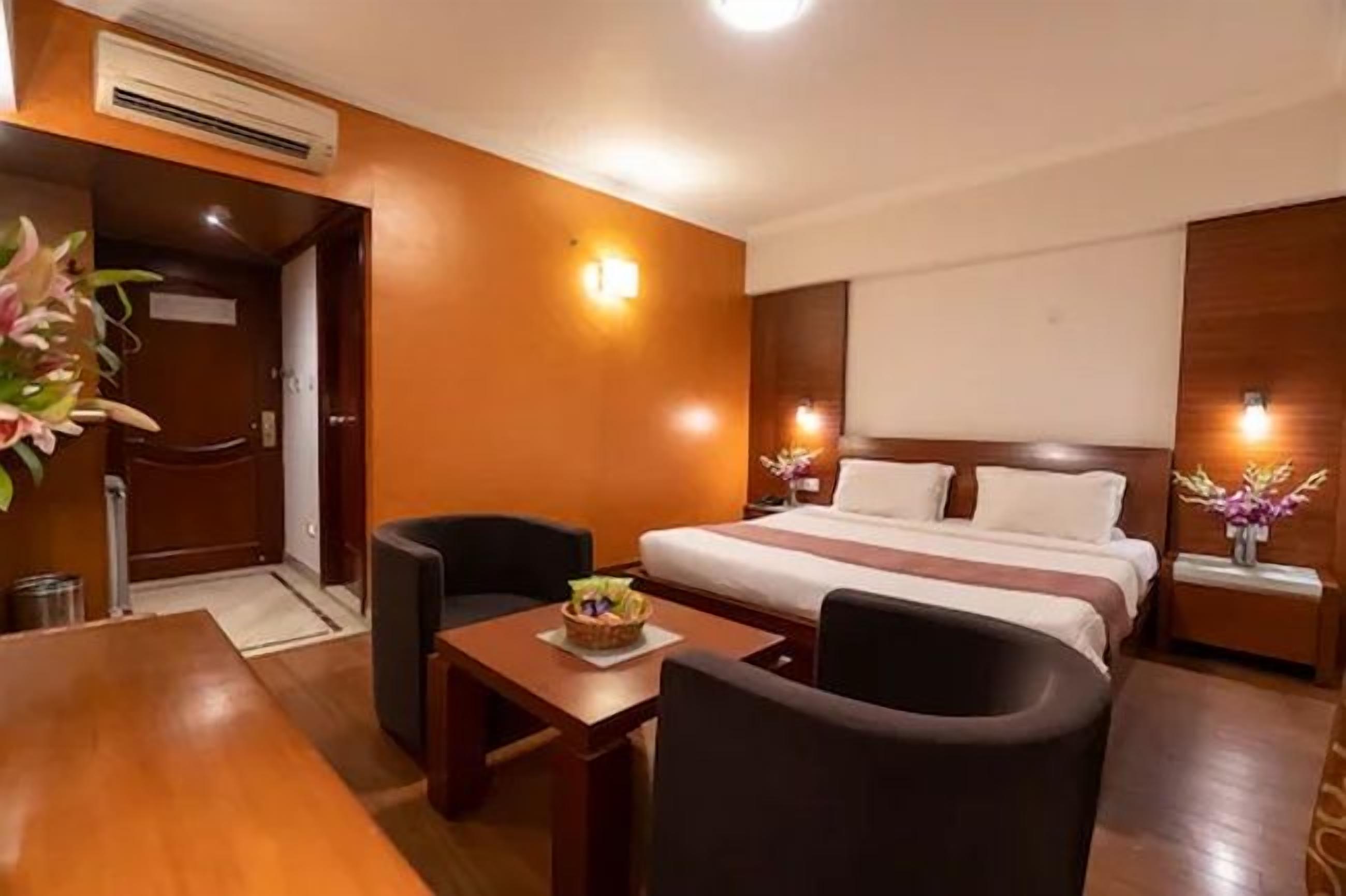 A hotel room with a bed, a desk, a chair, and a small table with a fruit bowl.