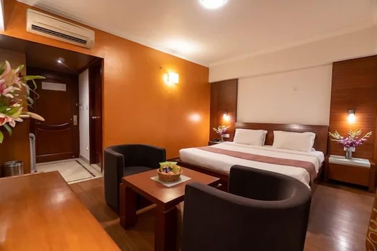 A hotel room with a bed, a desk, a chair, and a small table with a fruit bowl.