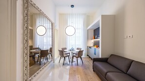 A modern living room with a large mirror, a dining area with a round table and chairs, and a kitchen area with cabinets and a countertop. - Caracolé Luxury Suites (Naples)