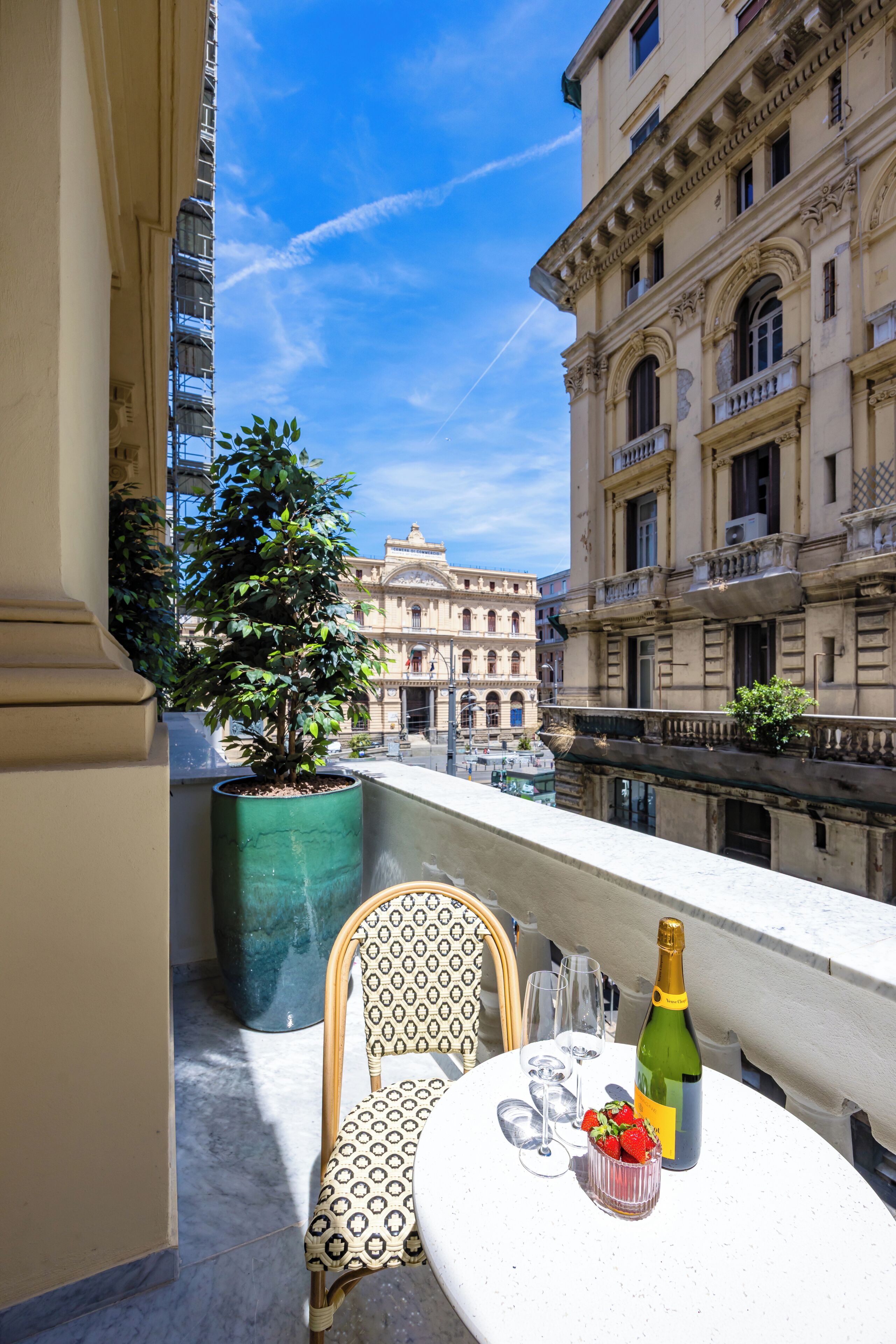 A balcony with a table, a chair, a bottle, and a bowl of strawberries.