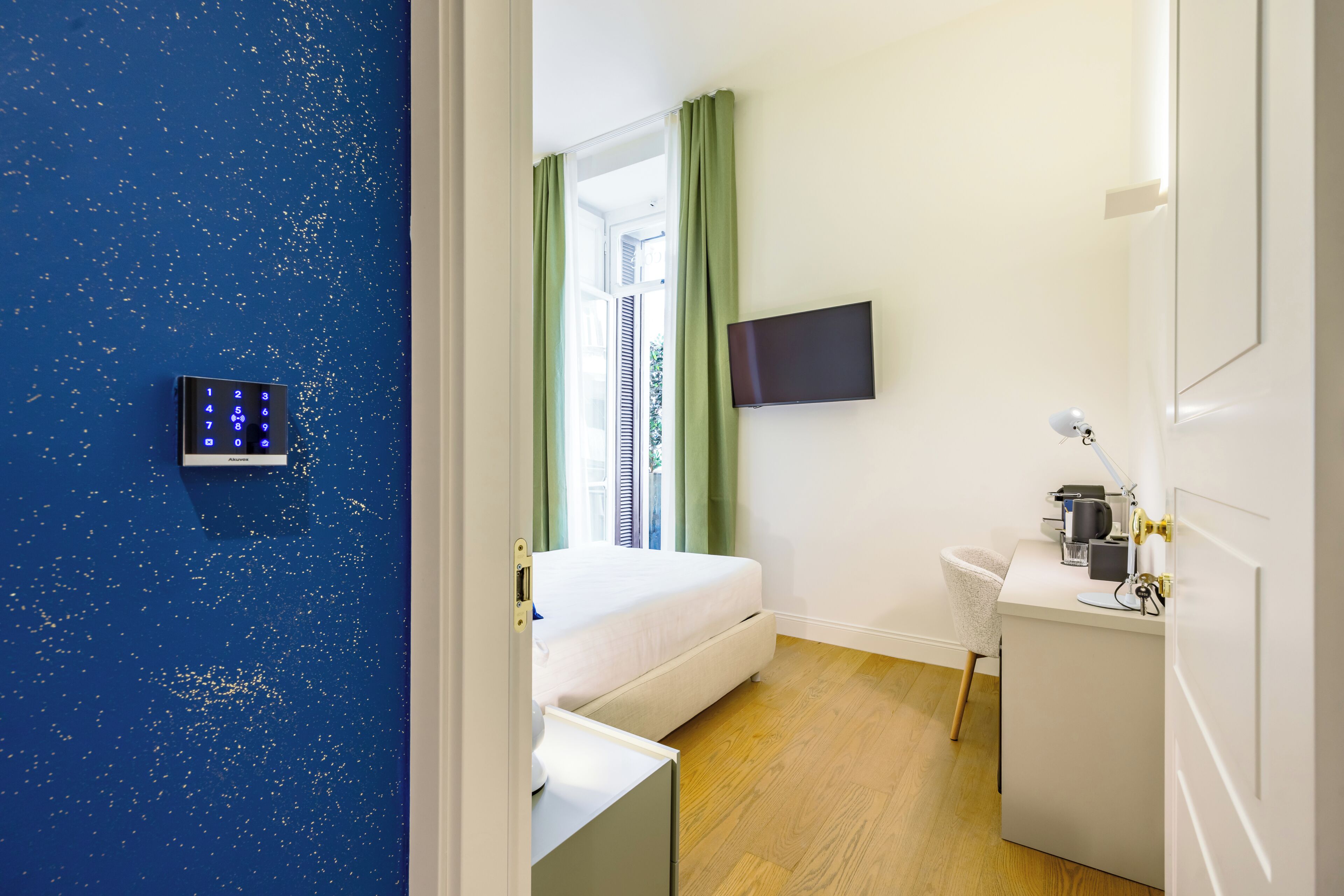 A hotel room with a bed, a desk, a TV, and a control panel on the wall.