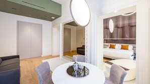 A modern hotel room with a round dining table, a large mirror, and a separate living area with a sofa and a bed. - Caracolé Luxury Suites (Naples)