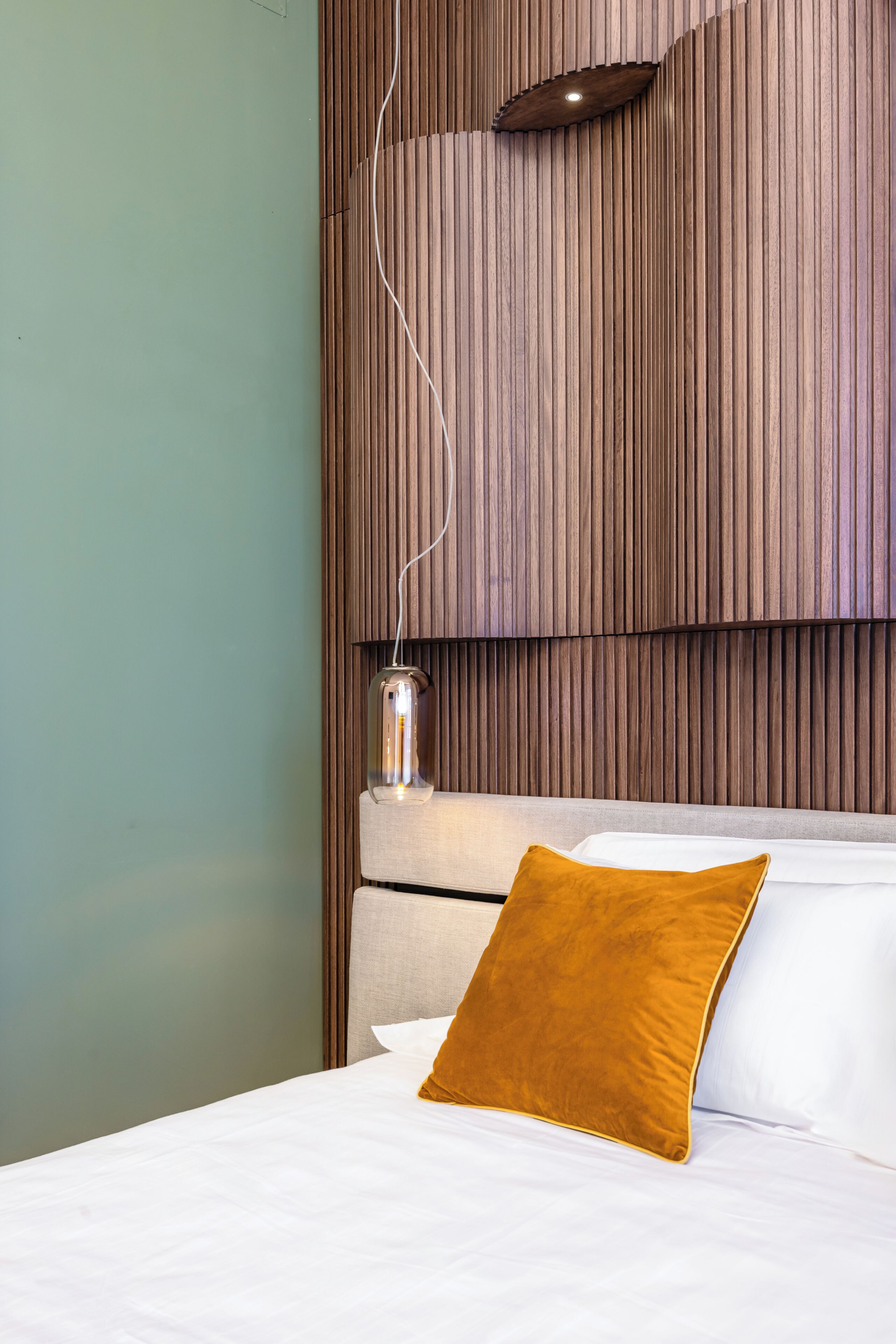 A hotel room with a bed, a headboard, a wall-mounted light fixture, and a bedside table with a lamp.