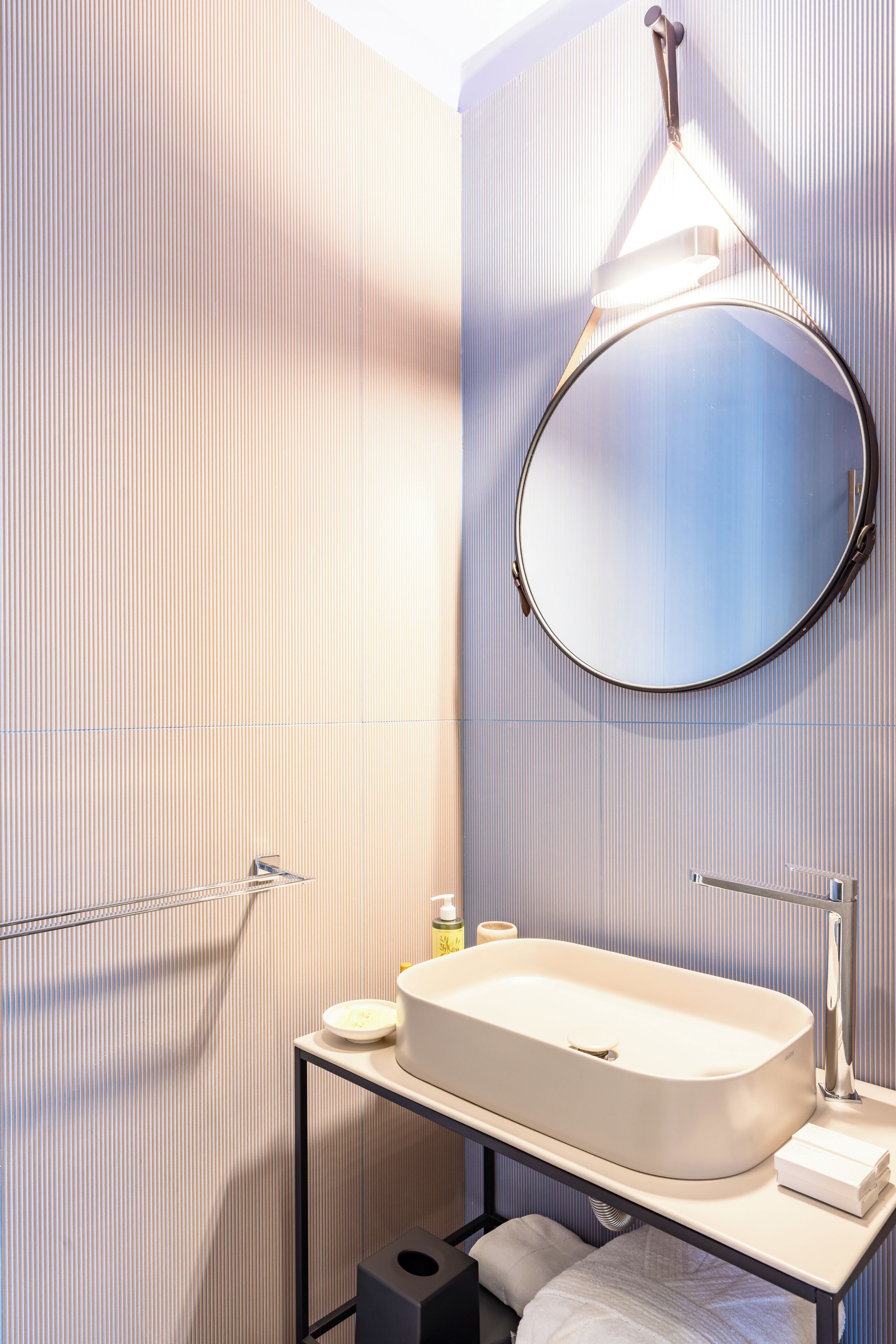Une salle de bain moderne avec un lavabo sur pied, un miroir rond et un porte-serviettes.