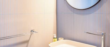 Une salle de bain moderne avec un lavabo sur pied, un miroir rond et un porte-serviettes.