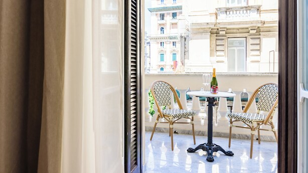 A balcony with two wicker chairs, a small round table, and a bottle of champagne. - Caracolé Luxury Suites (Naples)