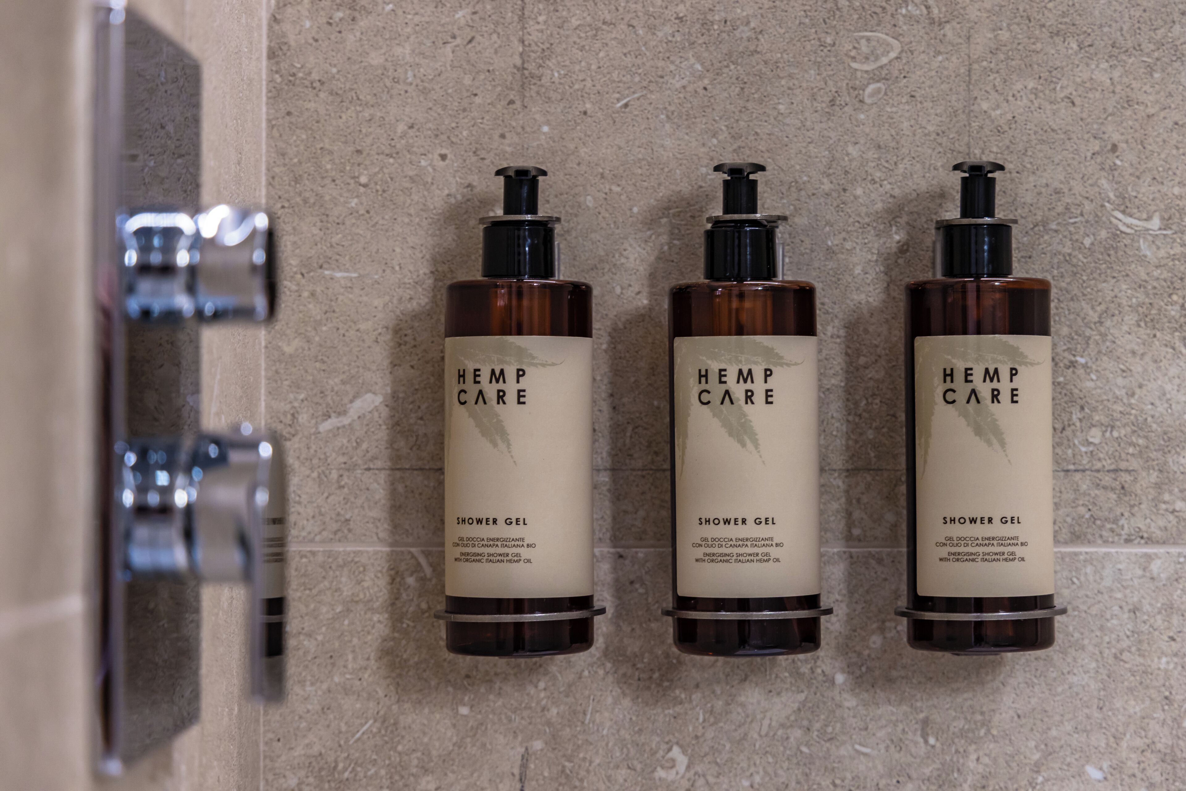 Three bottles of Hemp Care shower gel on a textured wall.
