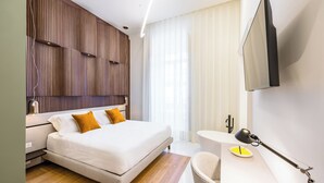 A modern hotel room with a bed, bedside table, lamp, and a flat-screen TV mounted on the wall. - Caracolé Luxury Suites (Naples)