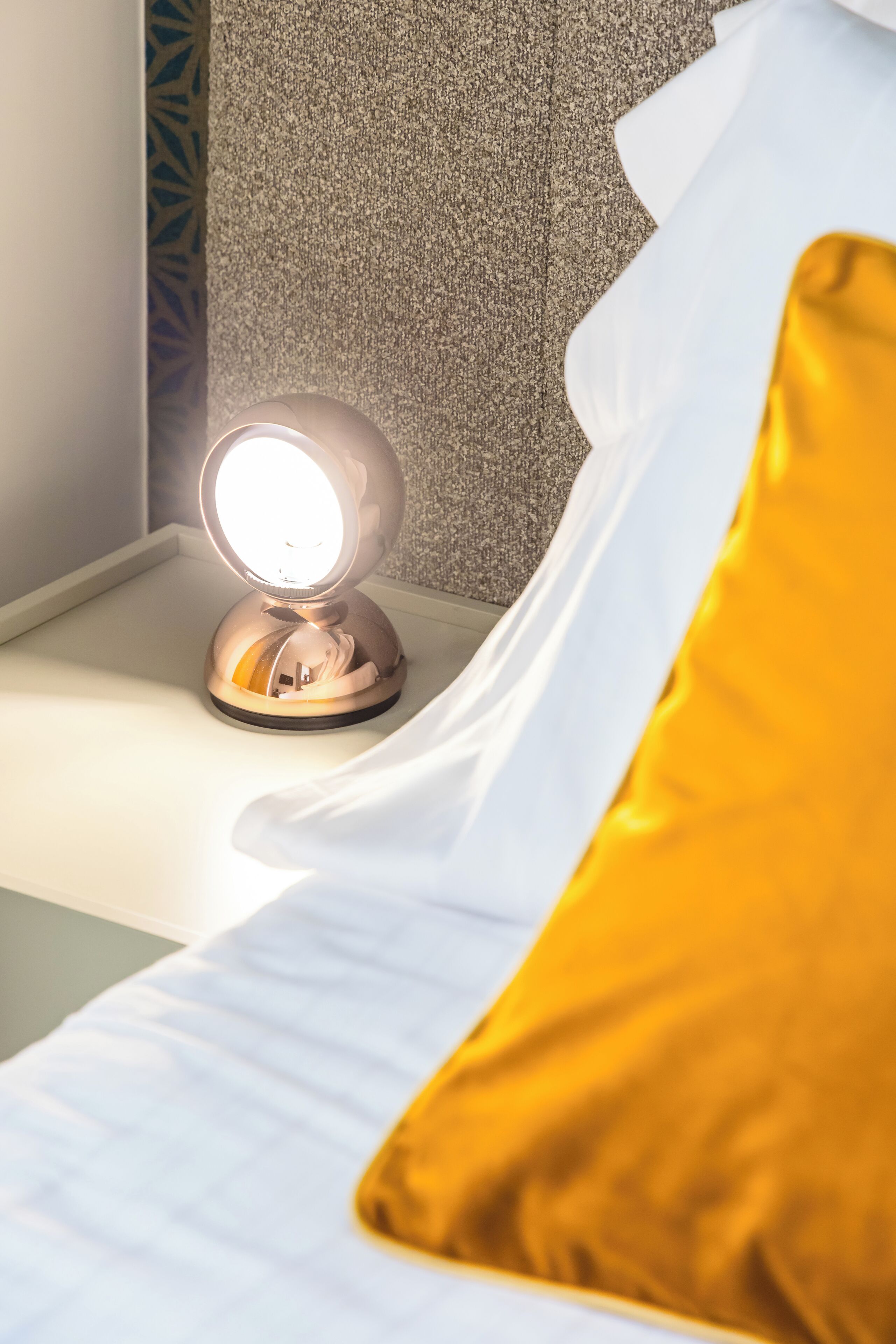 A bed with a white headboard, a yellow pillow, and a round mirror with a light on top.