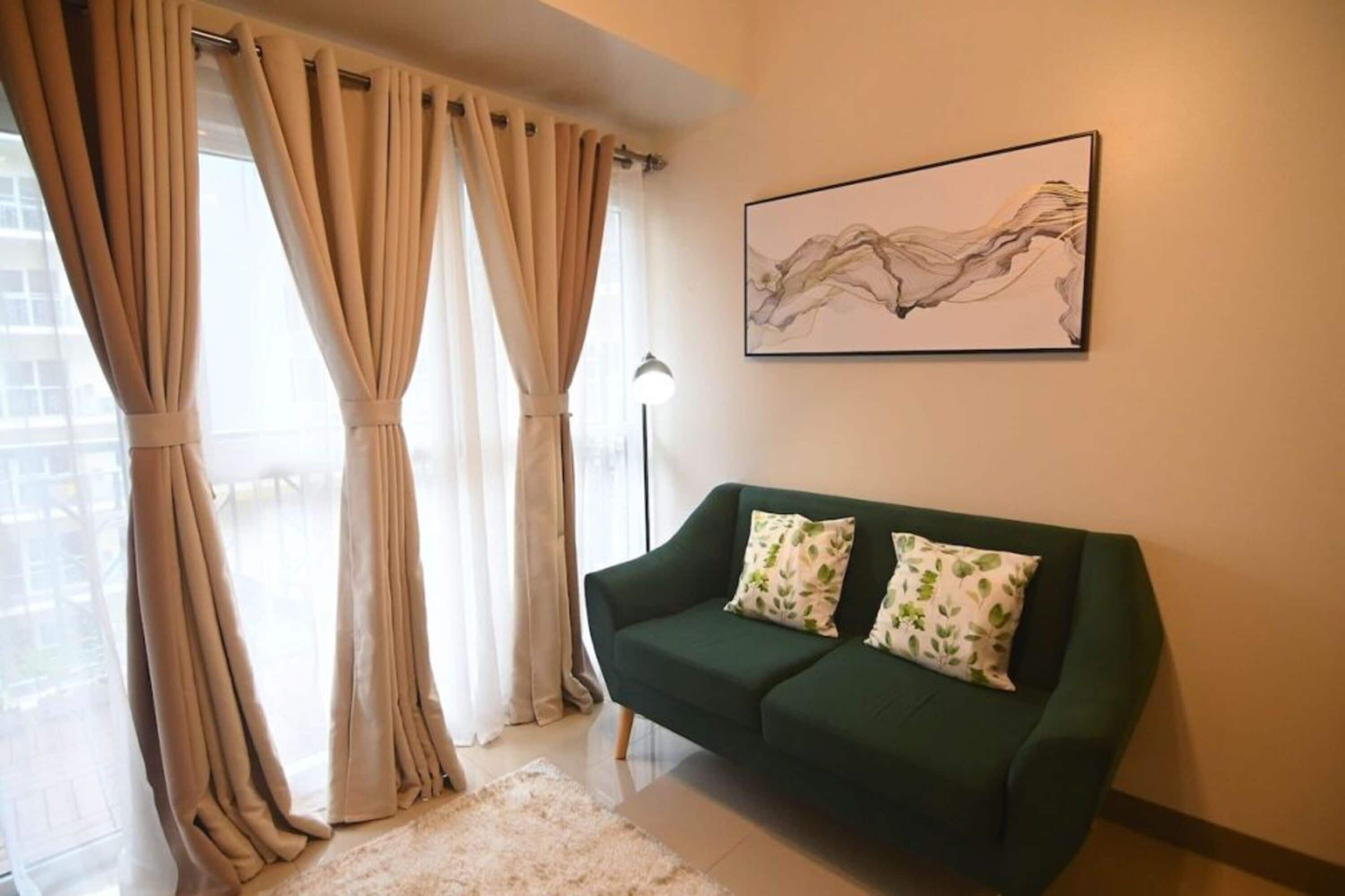 A living room with a green sofa, beige curtains, and a wall-mounted abstract painting.