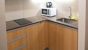 A compact kitchen with wooden cabinets, a built-in microwave, a kettle, and a sink. - Kuya Awens Staycation Unit 15K (Parañaque)