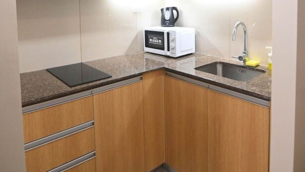 A compact kitchen with wooden cabinets, a built-in microwave, a kettle, and a sink. - Kuya Awens Staycation Unit 15K (Parañaque)
