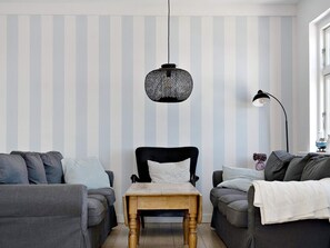 Ein Zimmer mit gestreifter Tapete, einem schwarzen Sessel, einem Holztisch und zwei grauen Sofas.