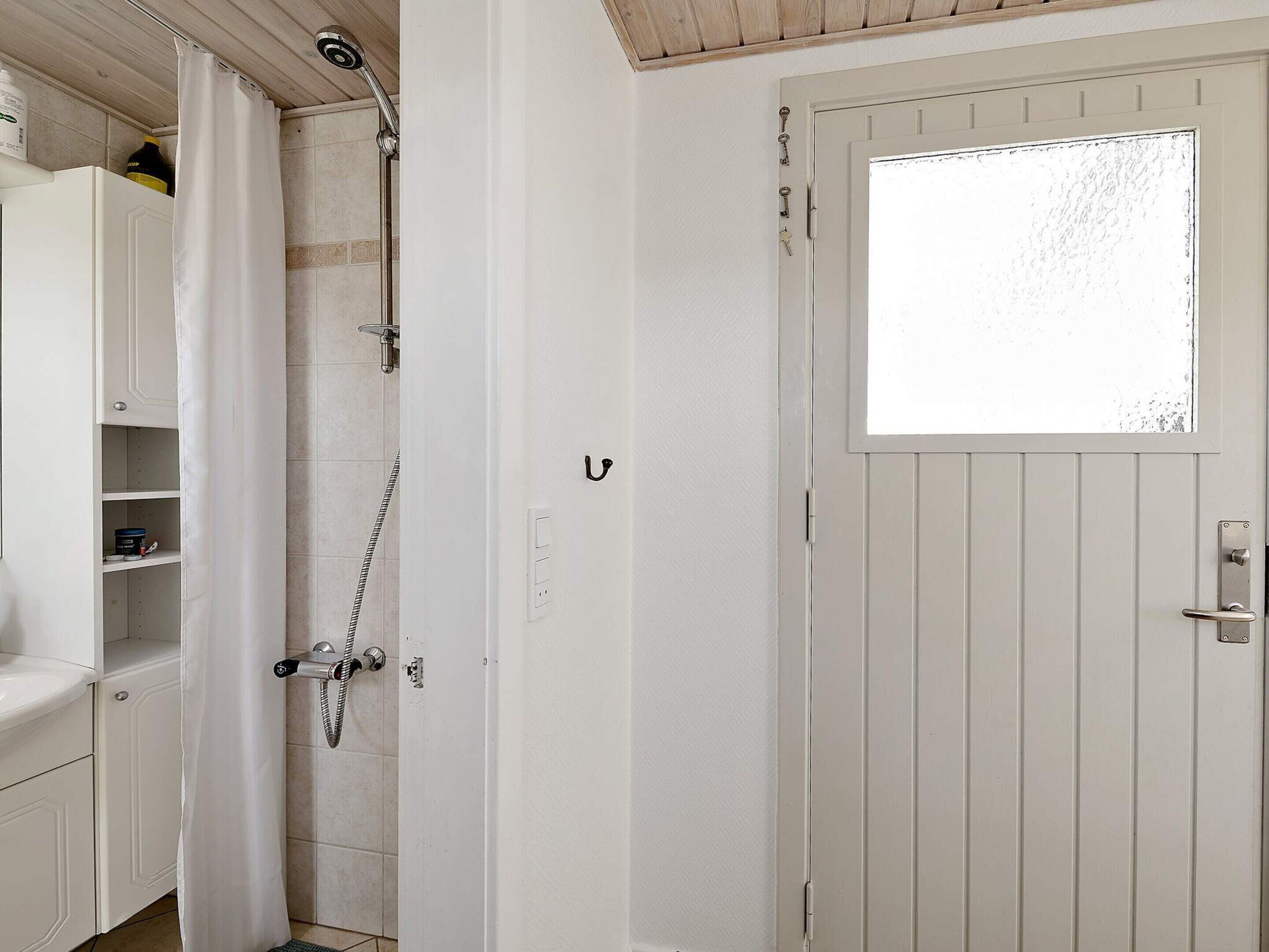 Een badkamer met een douche, een witte deur met raam, en een wit kastje met planken.