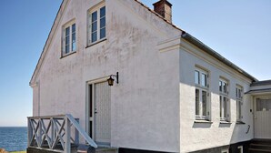 A two-story building with a white facade, a set of stairs leading to the entrance, and a view of the sea in the background. - 5 Star Holiday Home in Svaneke (Svaneke)