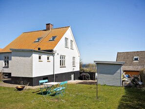 Ein Haus mit geneigtem Dach, einer kleinen angebauten Garage und einem Rasen mit Gartenmöbeln.