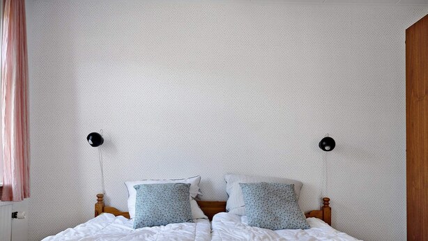 A bedroom with a bed, two bedside lamps, and a window with curtains. - 5 Star Holiday Home in Svaneke (Svaneke)