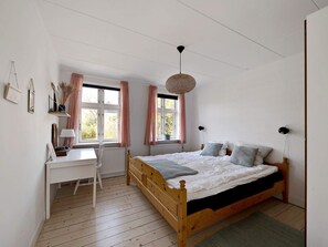 A bedroom with a wooden bed, a desk, and a window with curtains. - 5 Star Holiday Home in Svaneke (Svaneke)