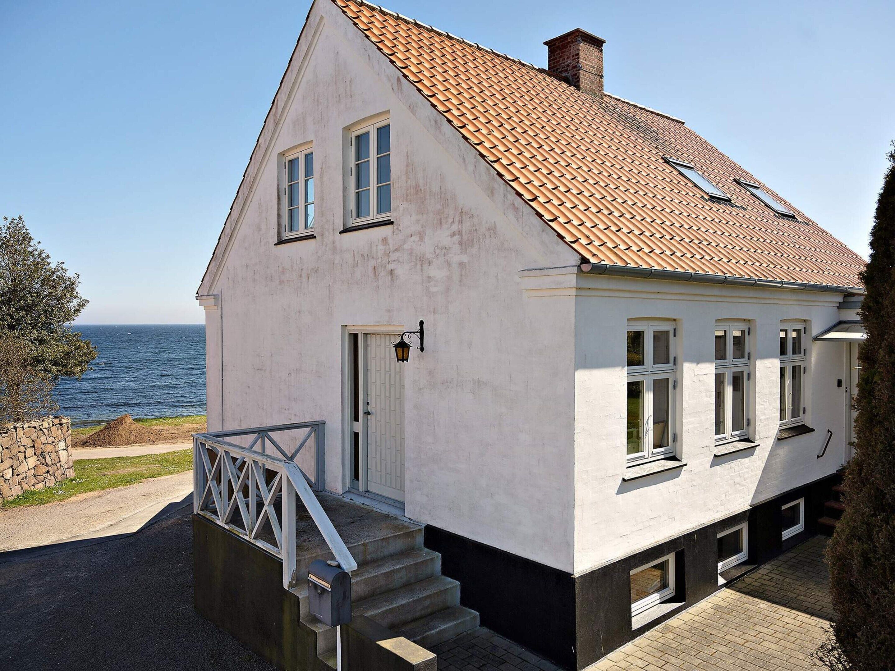 A two-story house with a sloped roof, a stone wall, and a view of the sea.