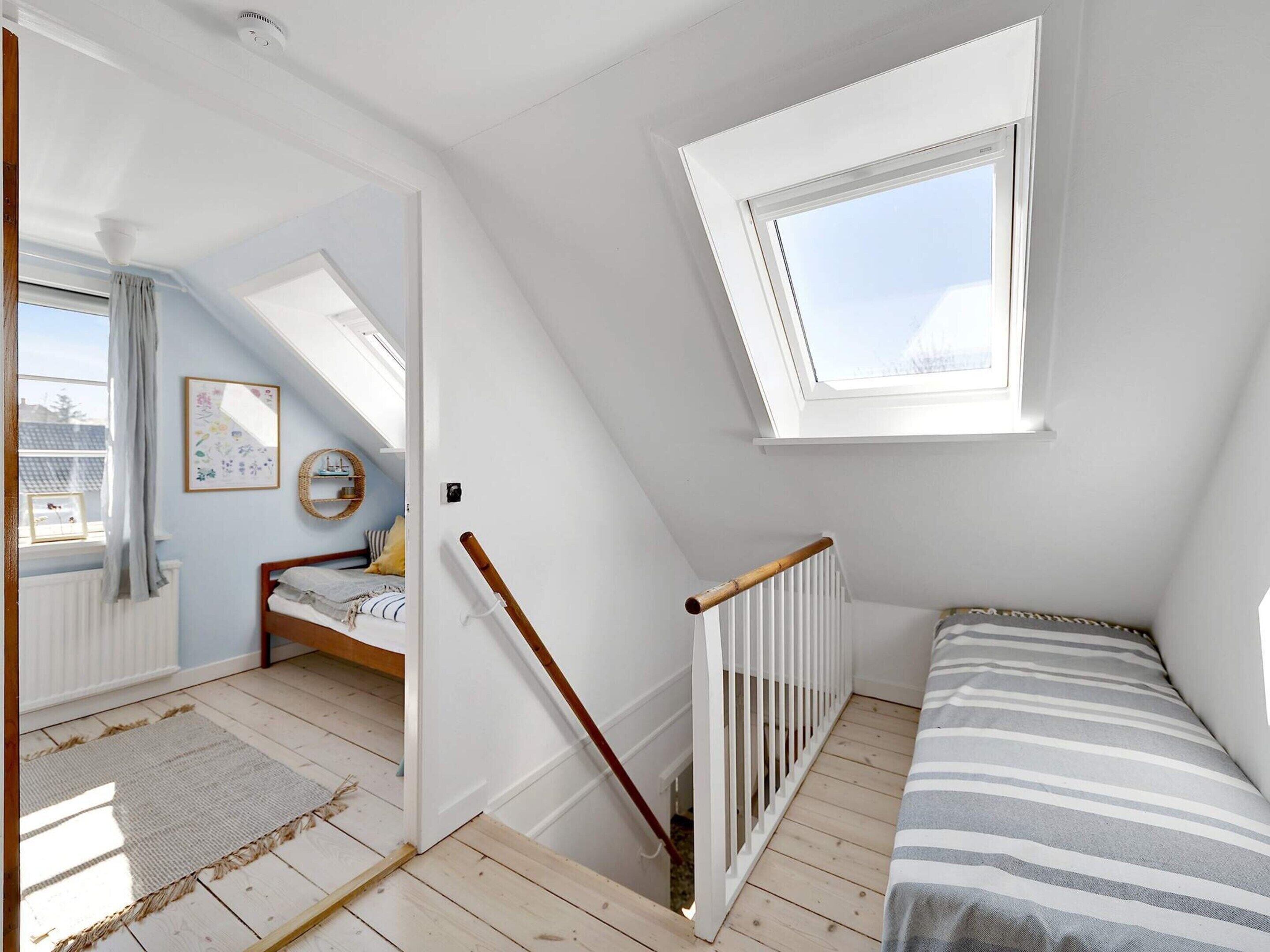 A room with a sloped ceiling, a bed, a window, and a door leading to another room.