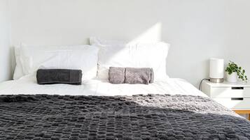A bed with a textured blanket, white pillows, and a bedside table with a lamp and a plant.