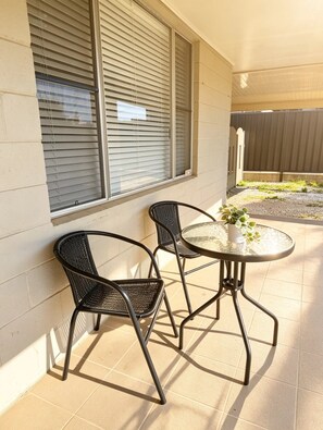 An outdoor patio with two chairs and a table, a potted plant, and a view of a gated area. - Spacious Cosy Family & Pet-Friendly Home with Large Backyard (Dubbo)