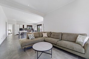 A modern living room with a sectional sofa, a round coffee table, and a view into the kitchen area.