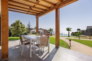Un patio exterior con mesa y sillas, con vista a una piscina y follaje.