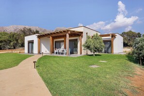 A modern house with a patio, a small garden, and a mountain backdrop.