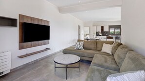 En moderne stue med et fladskærms-tv på væggen, en sofa, et sofabord og et køkken i baggrunden.