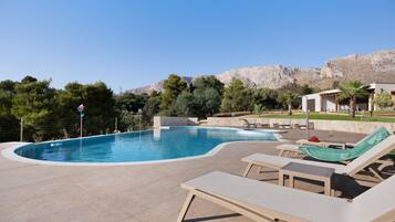 A swimming pool with lounge chairs, a small deck area, and a mountainous backdrop.