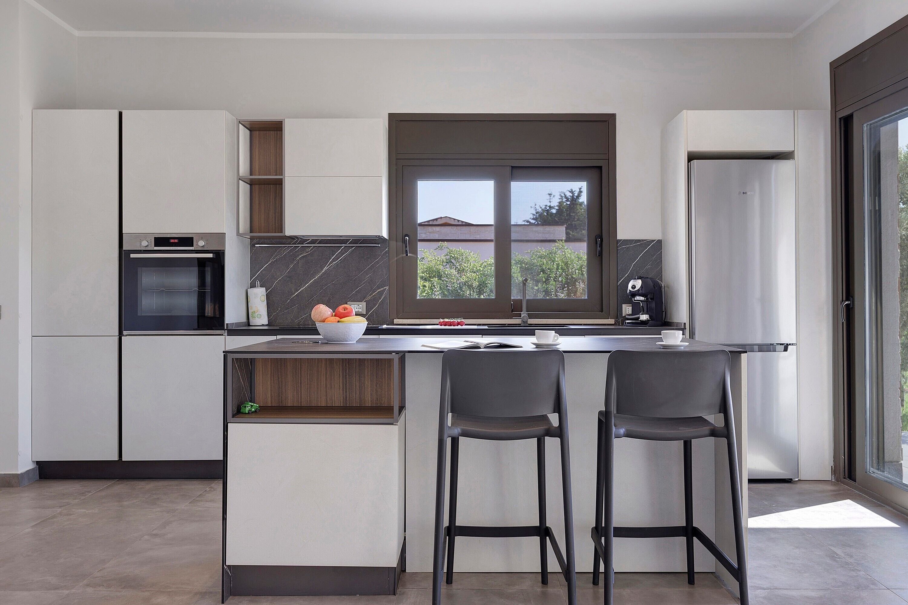 A modern kitchen with a built-in oven, a coffee machine, and a refrigerator.