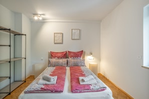 Ein Schlafzimmer mit einem Bett, zwei Wandleuchten, einem Heizkörper und einem Regalelement.