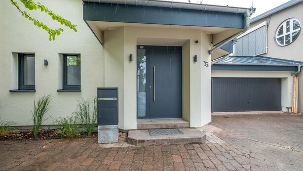Una casa moderna con una porta grigia, un piccolo portico e un garage.
