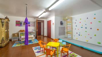 Une pièce avec un mur d’escalade, une table avec des chaises, un objet violet suspendu et une bibliothèque.
