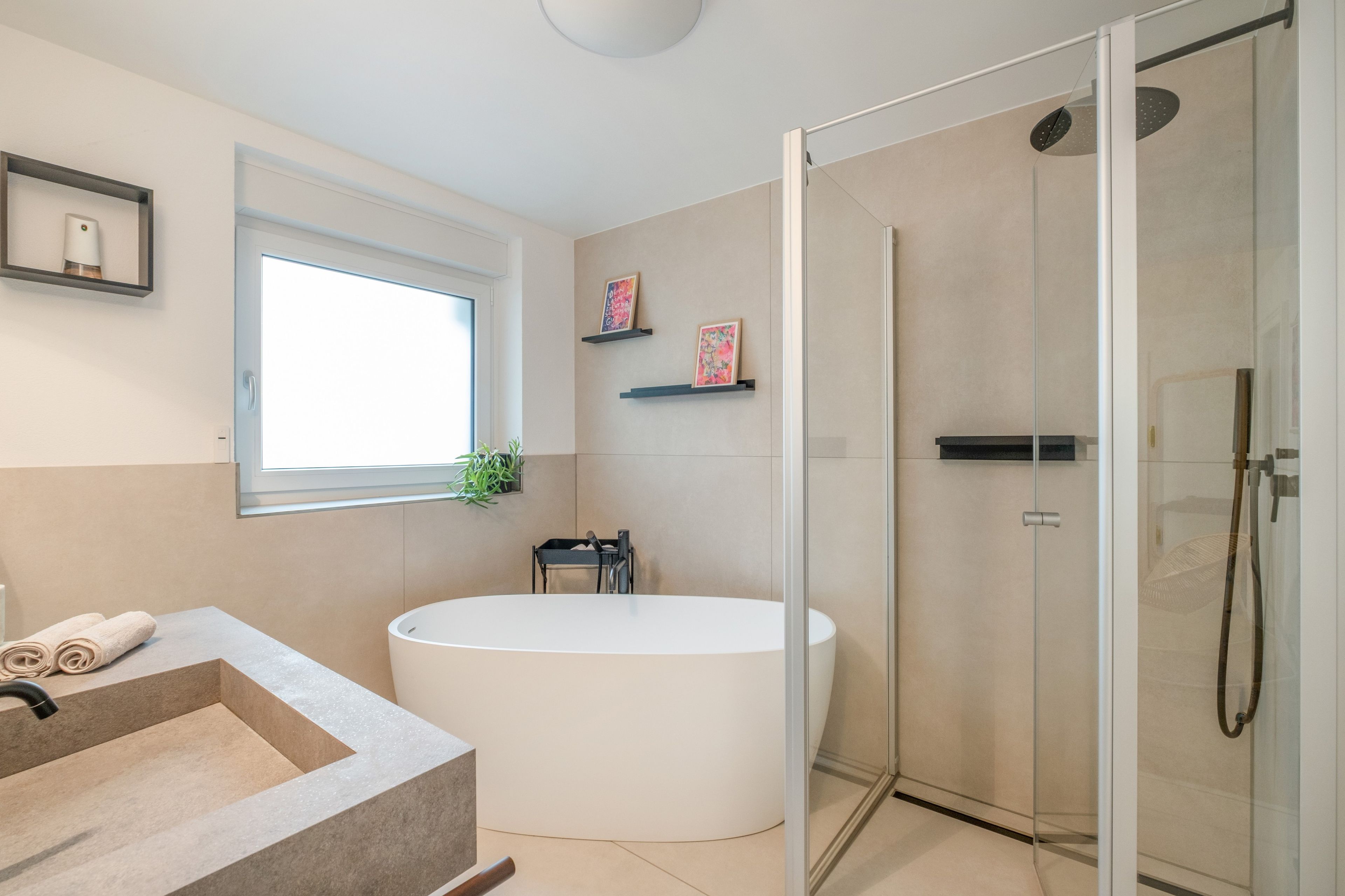 Un baño moderno con una bañera independiente, una ducha con cerramiento de vidrio y una ventana que proporciona luz natural.