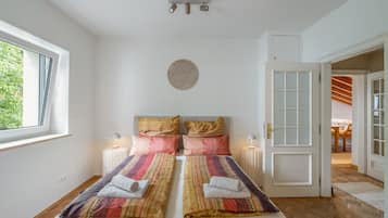 Une chambre à coucher avec un lit, deux lampes de chevet, un élément de décoration circulaire fixé au mur, et une vue sur l’extérieur par une fenêtre.