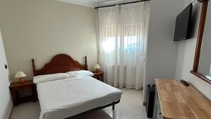 Hotellihuone, jossa on sänky, yöpöydät, työpöytä, televisio ja kattotuuletin.