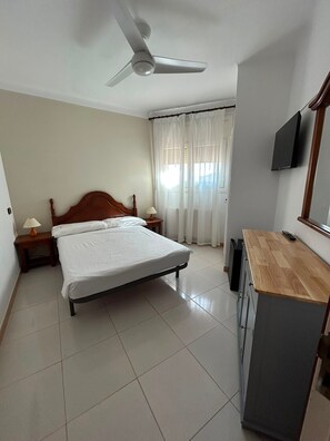 Une chambre d’hôtel équipée d’un lit, de tables de chevet, d’un bureau, d’une télévision et d’un ventilateur de plafond.