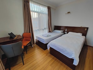 Ein Hotelzimmer mit zwei Betten, einem Schreibtisch mit Stuhl und einem fensterbepflanzten Fenster.