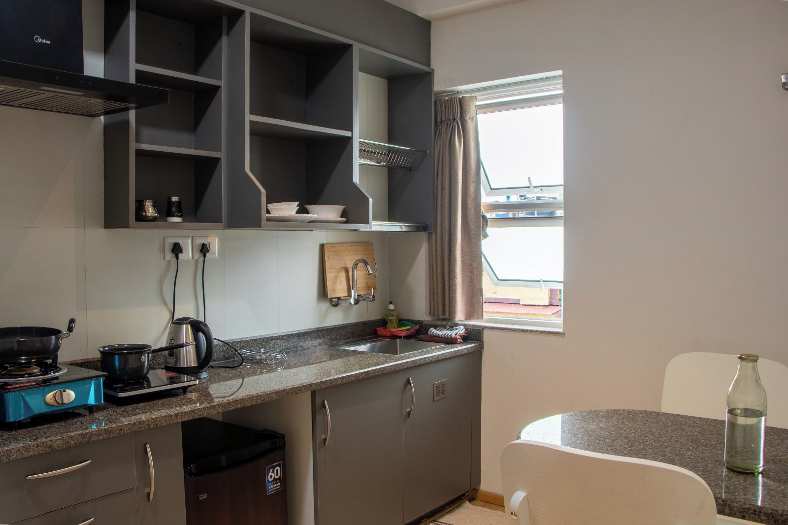 A modern kitchen with grey cabinets, a stainless steel range hood, and a window with curtains.