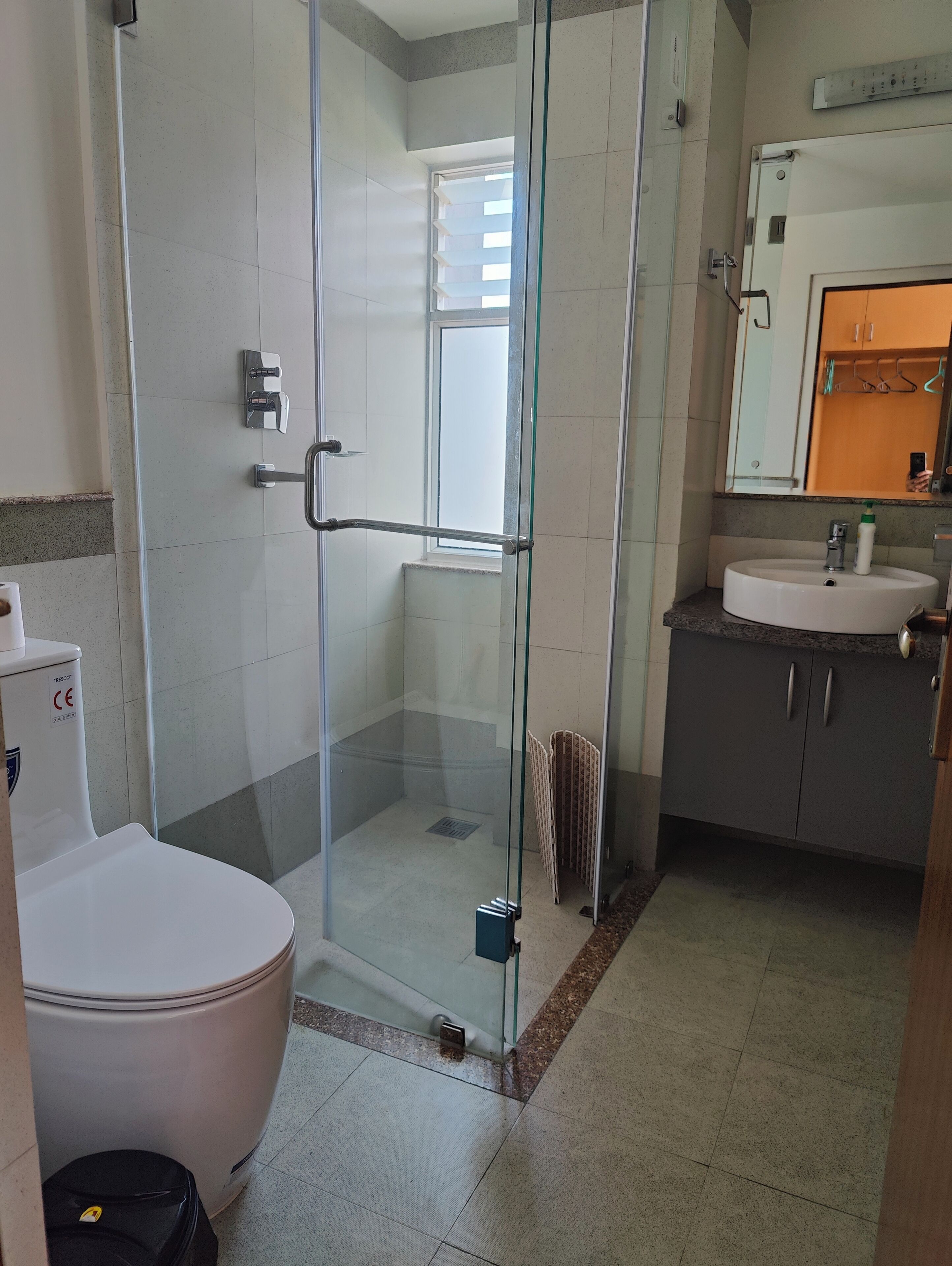 A bathroom with a glass-enclosed shower, a toilet, and a sink with a mirror above it.