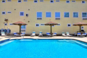 A swimming pool with lounge chairs and umbrellas, surrounded by a building with multiple windows and air conditioning units. - Beachgate Condo Suites And Hotel 432 1 Bedroom Condo (Port Aransas)