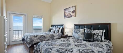 A bedroom with two beds, a ceiling fan, a painting, and a view through a door.