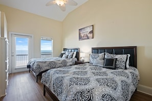 A bedroom with two beds, a ceiling fan, a painting, and a view through a door. - Kiki Beach 4 Bedroom Home (Port Bolivar)